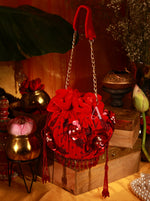Red decorative bag with floral details and beads on a wooden surface with decorative items.
