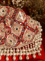 Decorative clutch with red base, silver embellishments, and pearl tassels on a blurred background.