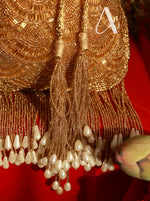 Gold beaded earring with tassels and pearls on a red background