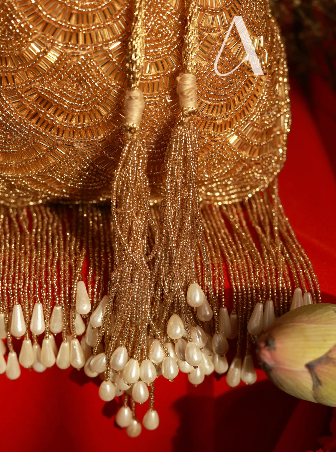 Gold beaded earring with tassels and pearls on a red background