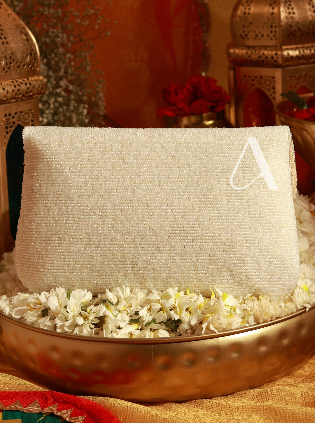 Decorative setting with a white cushion on a metallic tray, surrounded by flowers and lanterns.