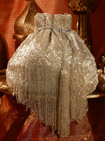 Silver beaded dress with fringe on a decorative stand against a red background