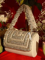 Beige handbag with crystal embellishments on a red surface with flowers in the background