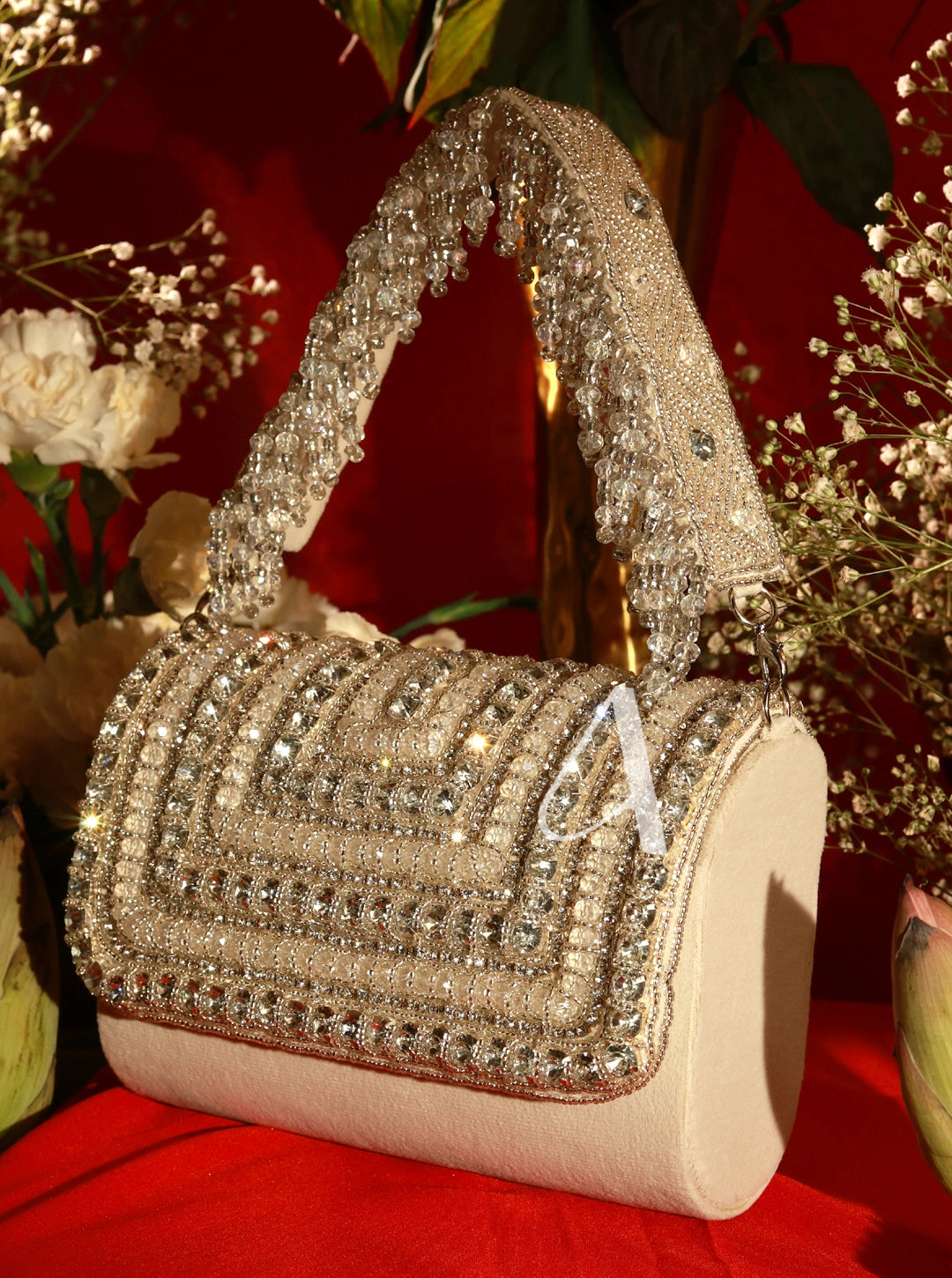 Beige handbag with crystal embellishments on a red surface with flowers in the background