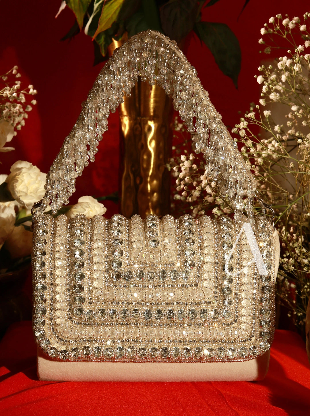 Decorative handbag with crystals on a red surface with flowers in the background