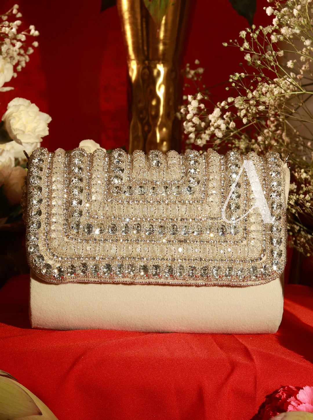Beige clutch bag with crystal embellishments on a red surface with flowers in the background