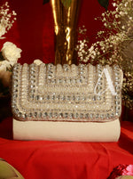 Beige clutch bag with crystal embellishments on a red surface with flowers in the background