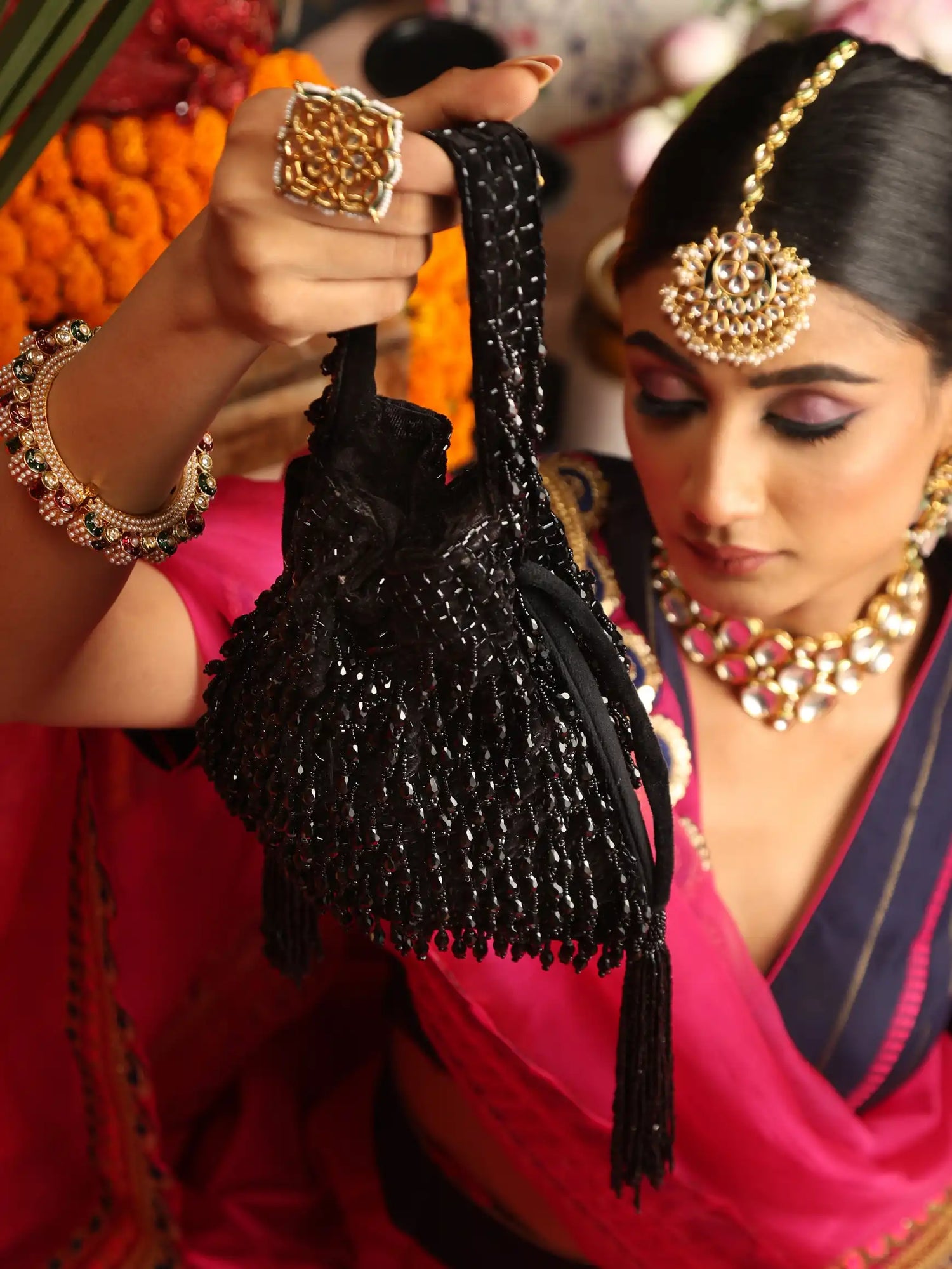 Woman in traditional attire holding a black beaded bag with intricate jewelry.