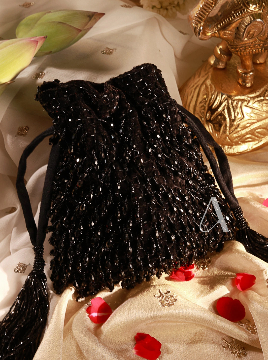 Black beaded drawstring bag on a decorative surface with red flowers and gold object.