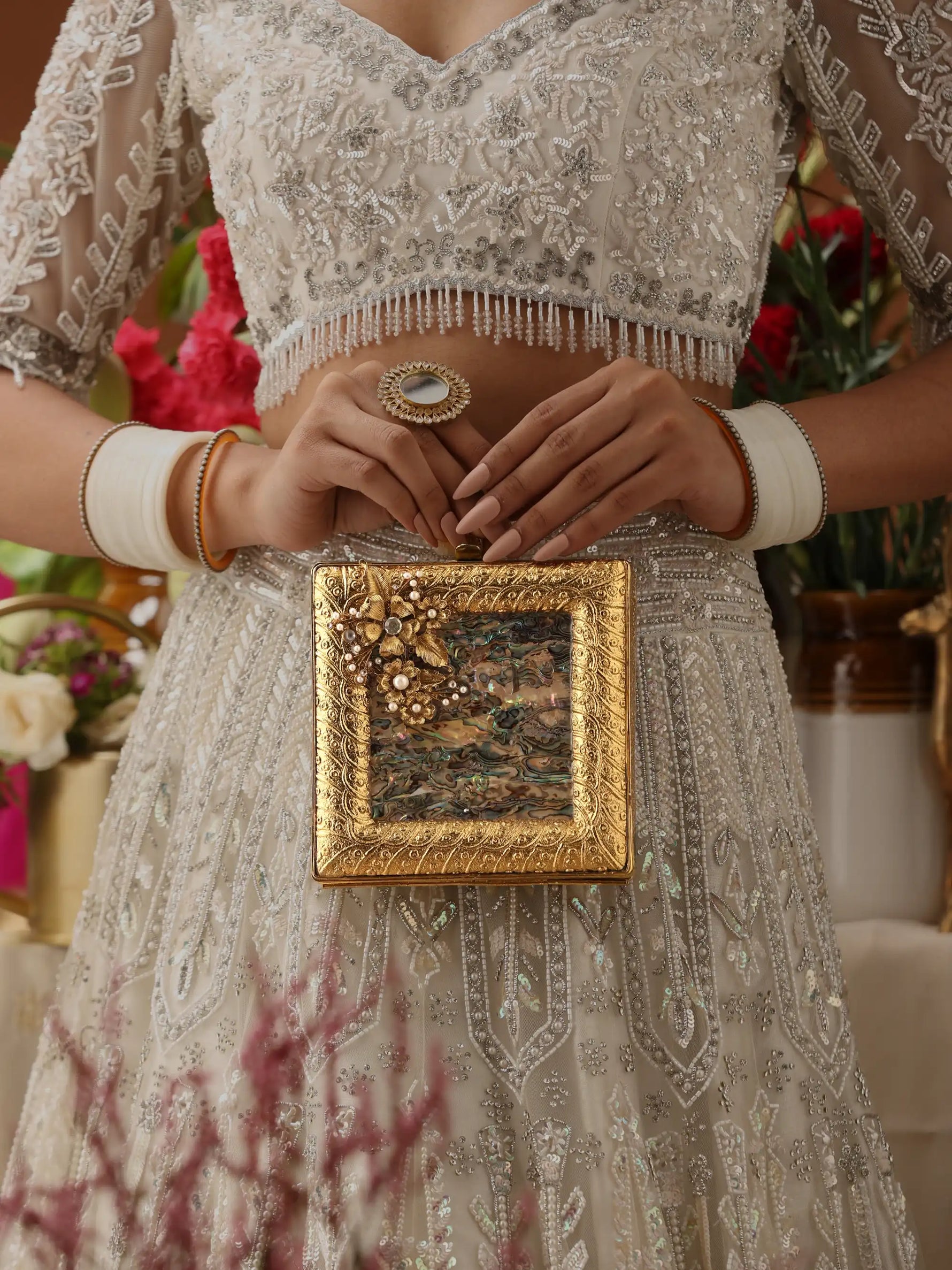 Person holding a gold frame with floral design, wearing an embroidered outfit.
