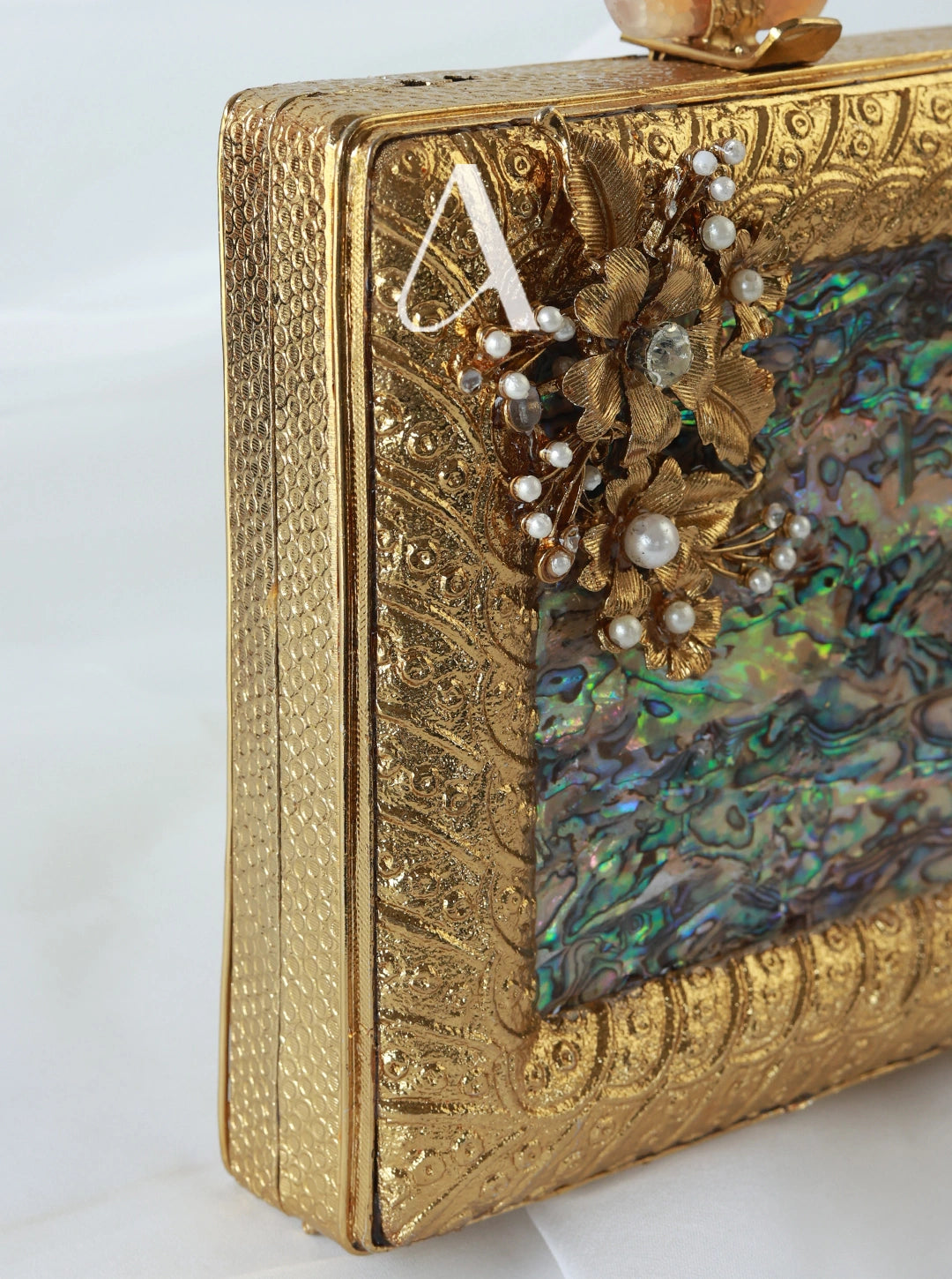 Gold clutch with floral design and abalone shell on a white background