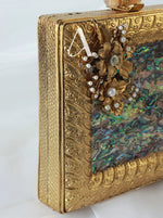 Gold clutch with floral design and abalone shell on a white background