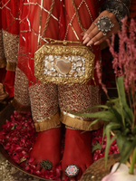 Person holding a gold and red handbag with intricate designs, wearing traditional attire.
