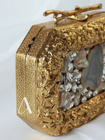 Gold clutch with textured surface and embedded stones on a white background