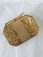 Gold clutch with intricate patterns on a white background