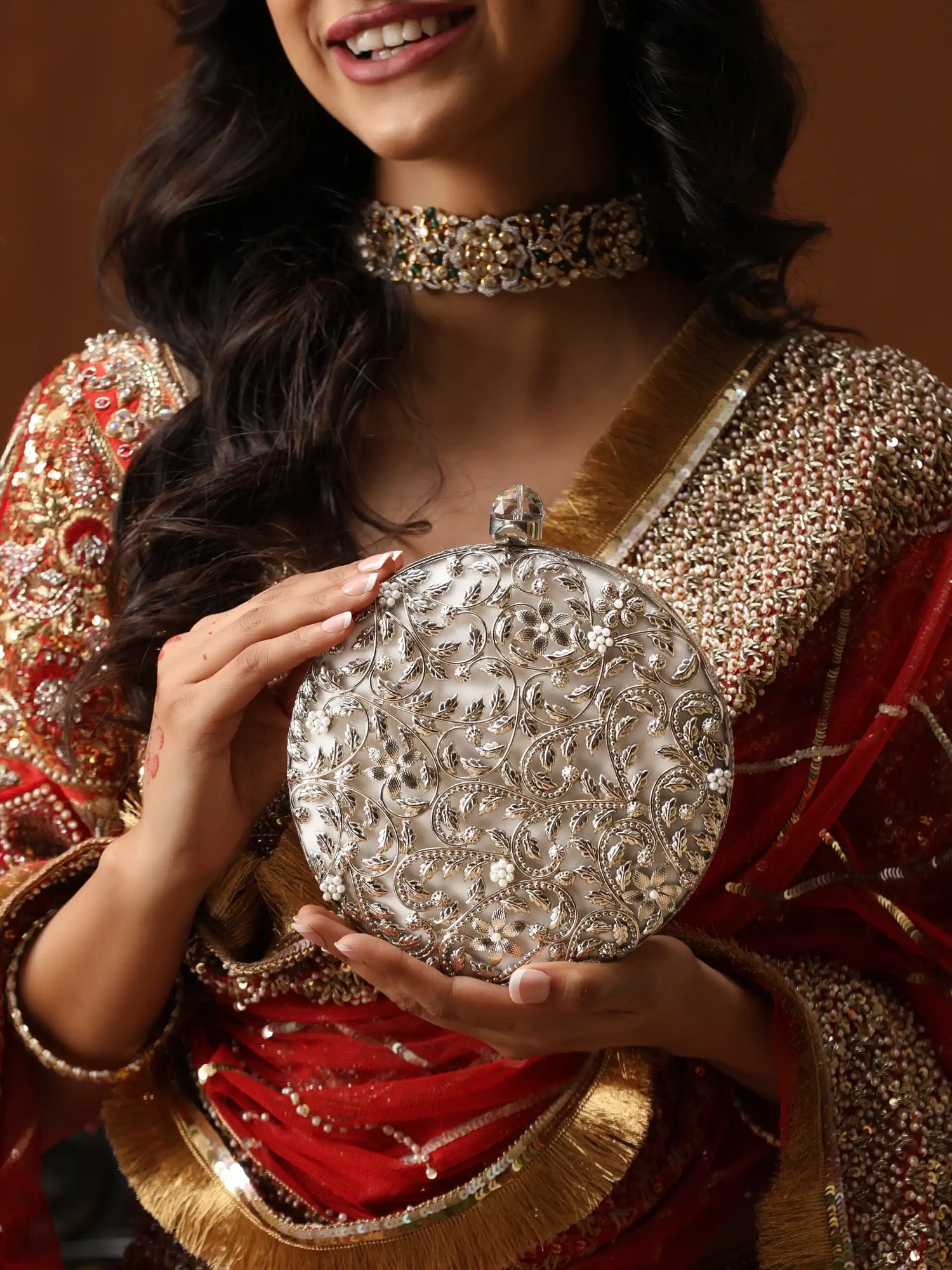 Woman in traditional attire holding a silver clutch with intricate designs.