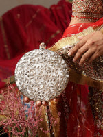 Person holding a silver clutch with intricate designs, wearing a red saree with gold border.