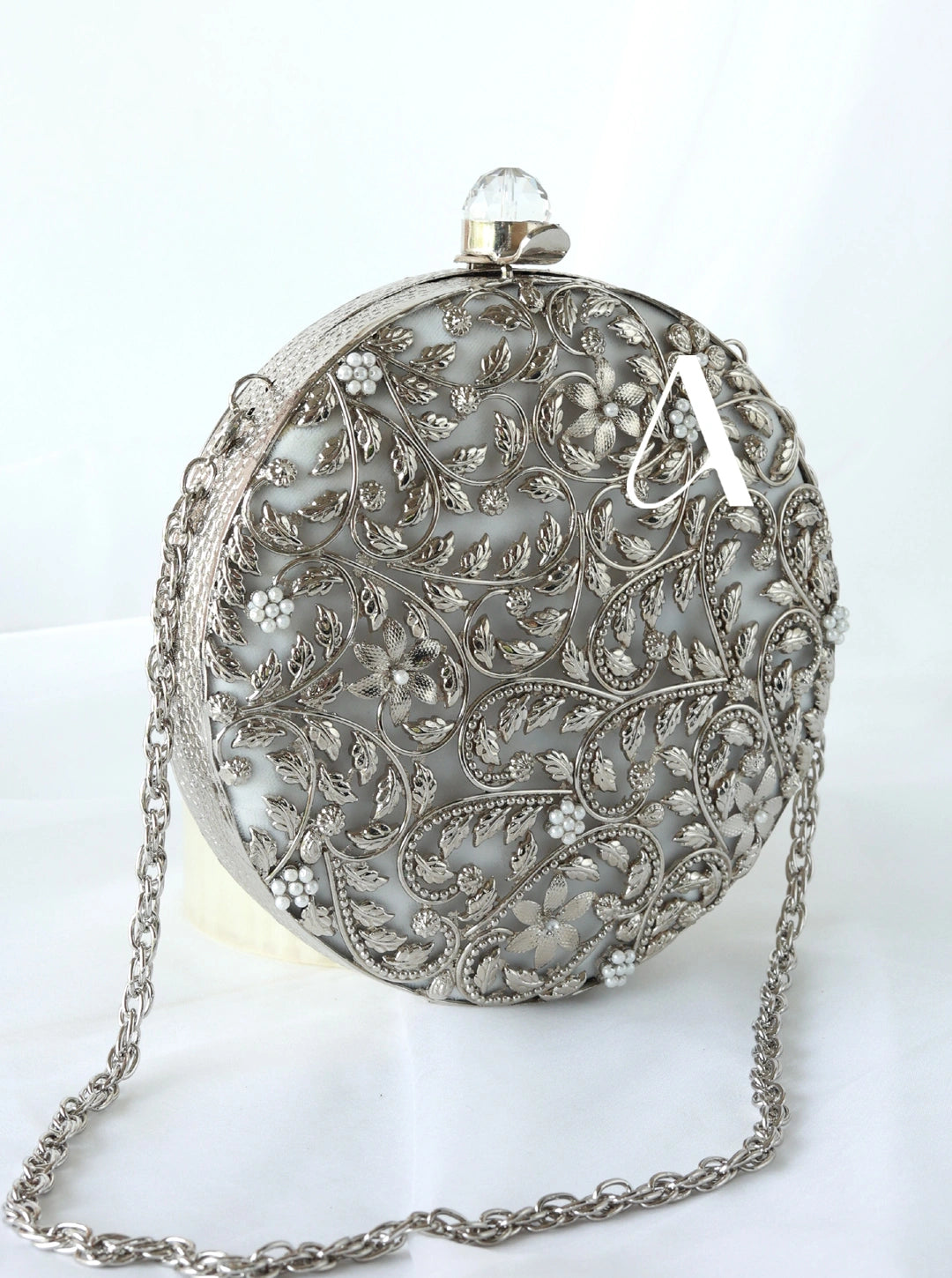 Silver evening bag with intricate floral patterns on a white background
