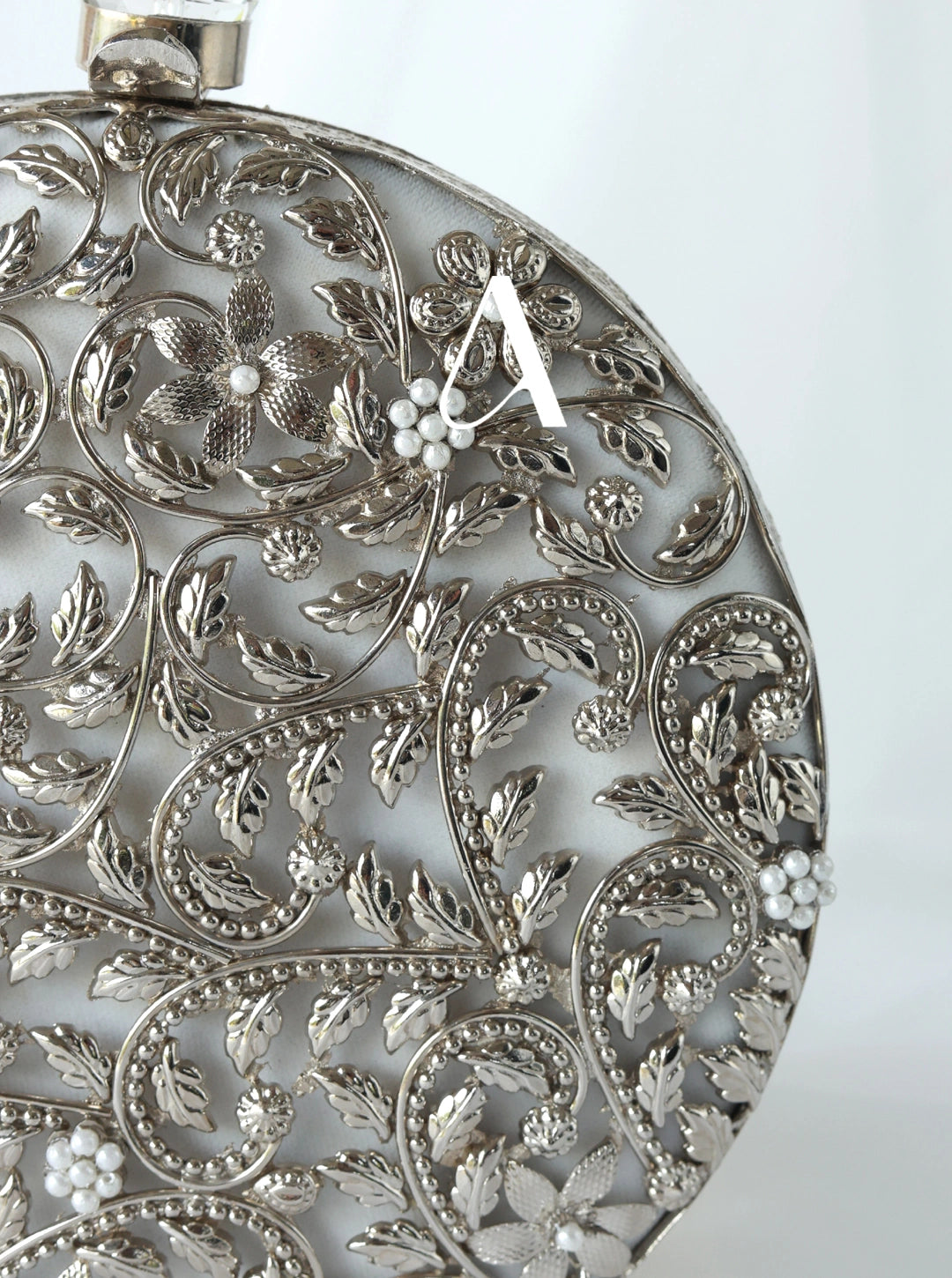 Close-up of a silver pendant with intricate floral patterns on a white background