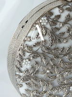 Decorative silver object with intricate leaf patterns and a central letter 'A'.