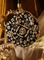 Decorative black clutch with gold floral patterns and a visible brand logo on a gold and white fabric background.