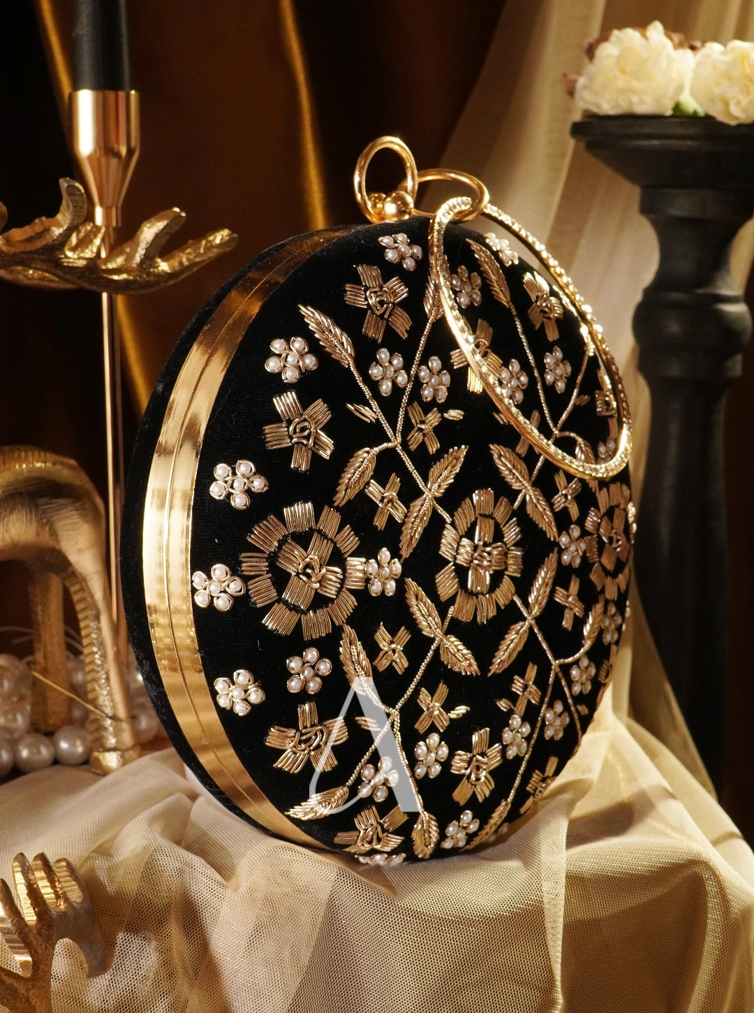 Black round clutch with gold floral embroidery on a decorative background