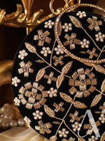 Black clutch with gold floral embroidery and pearl accents on a dark background
