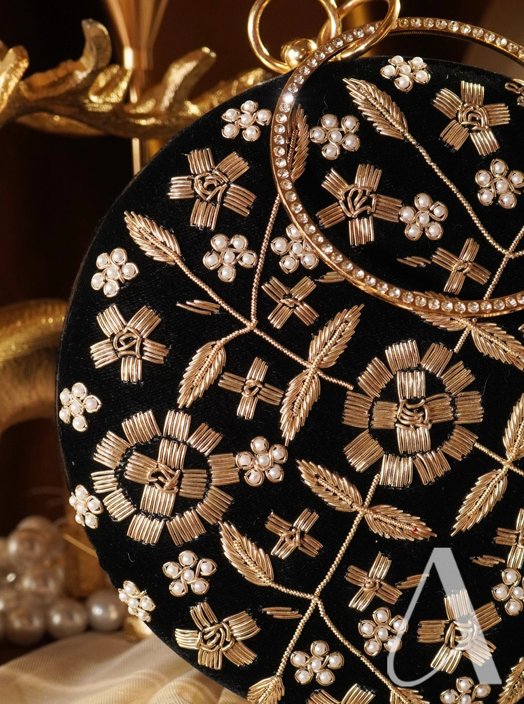 Black clutch with gold floral embroidery and pearl accents on a dark background
