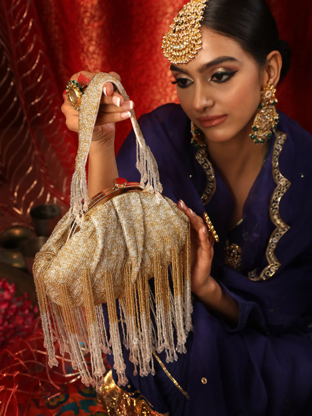 Woman holding a gold handbag with fringe details against a red background