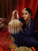 Woman in traditional attire holding a decorative bag against a red curtain background