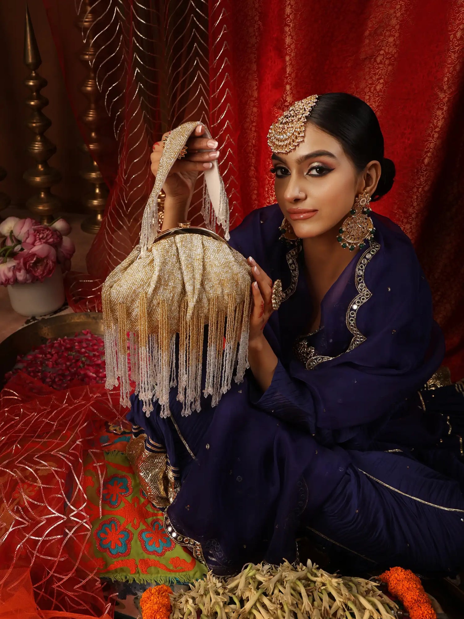 Woman in traditional attire holding a decorative bag against a red curtain background