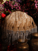 Decorative lampshade with fringe and beads on a dark background with flowers.