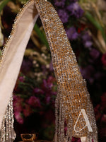 Gold beaded shoe with decorative strap featuring a letter 'A' against a blurred floral background