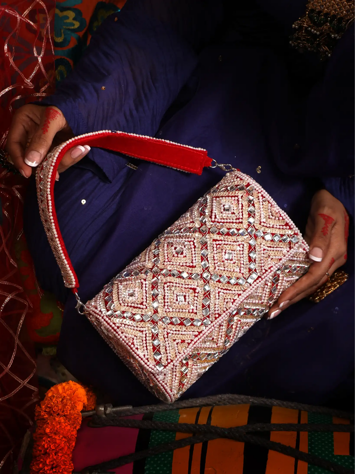 Person holding a decorative clutch with intricate patterns and red accents.