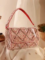 Decorative handbag with red and silver embellishments on a white fabric background