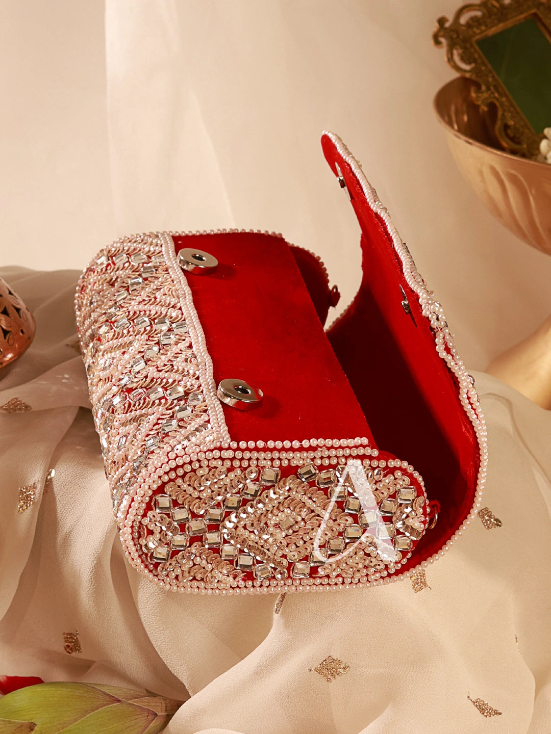 Red handbag with intricate silver detailing on a white fabric background