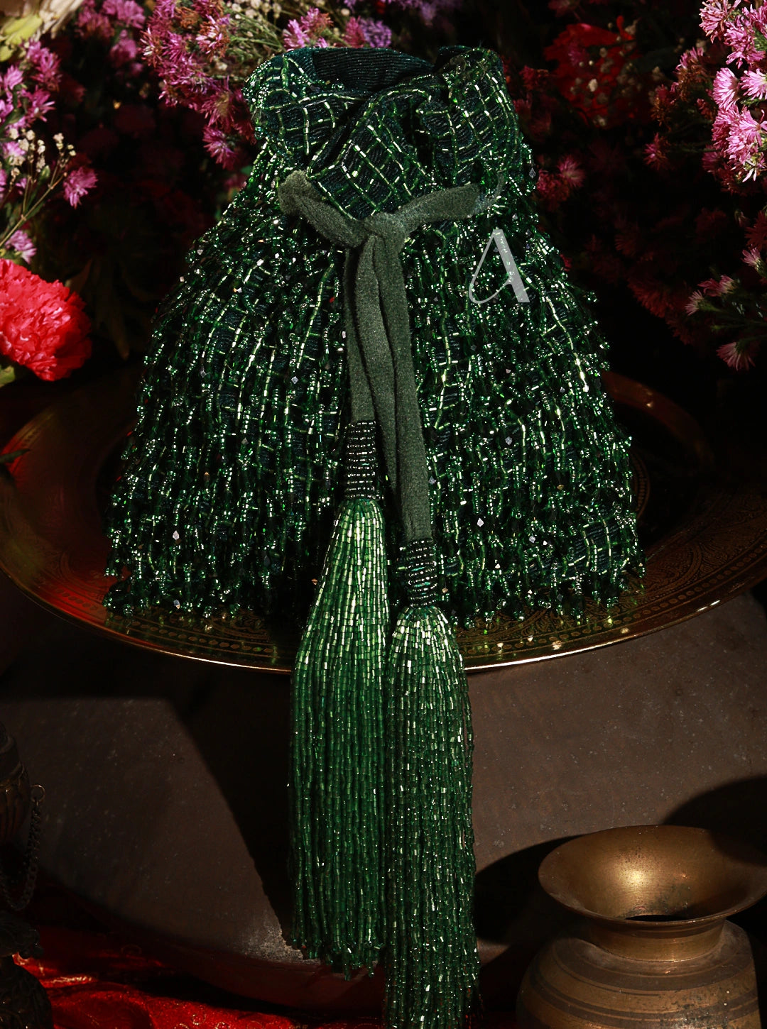 Green beaded bag with tassel on a reflective surface with flowers in the background