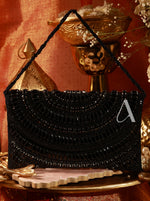Black beaded handbag with gold accents on a decorative stand against an orange wall.