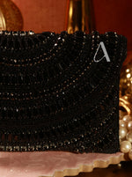 Black beaded clutch with a decorative 'A' on a pink surface