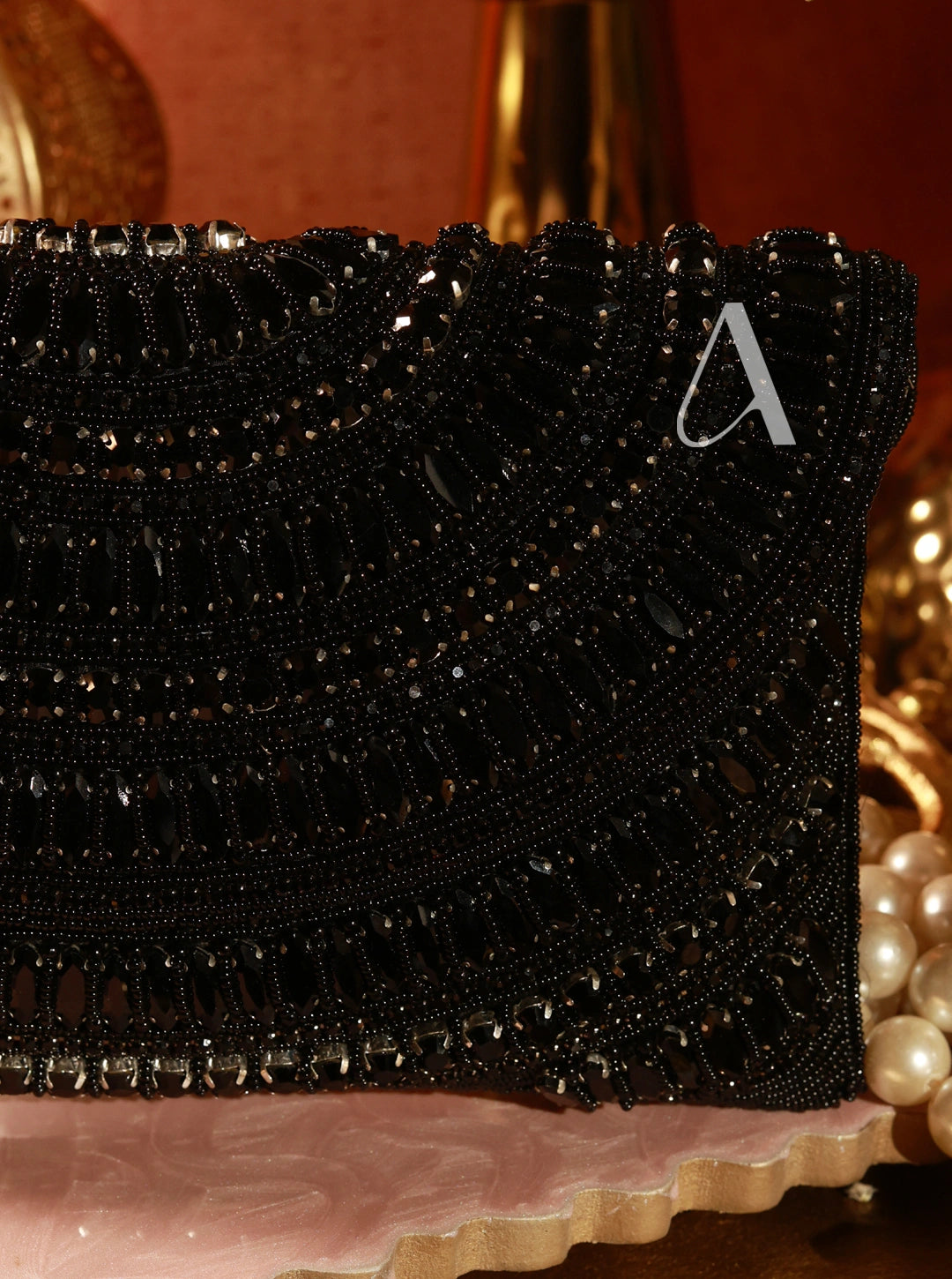 Black beaded clutch with a decorative 'A' on a pink surface