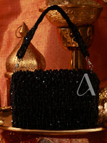Black beaded handbag on a decorative surface with gold accents