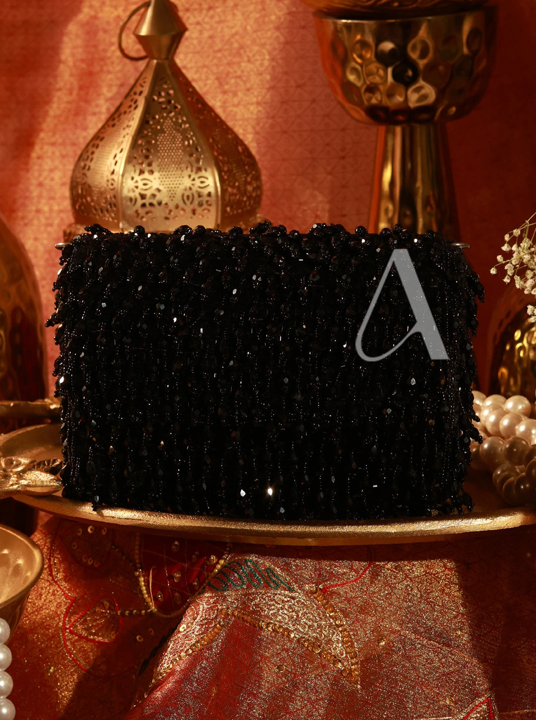 Black beaded clutch on a decorative table with gold and red background