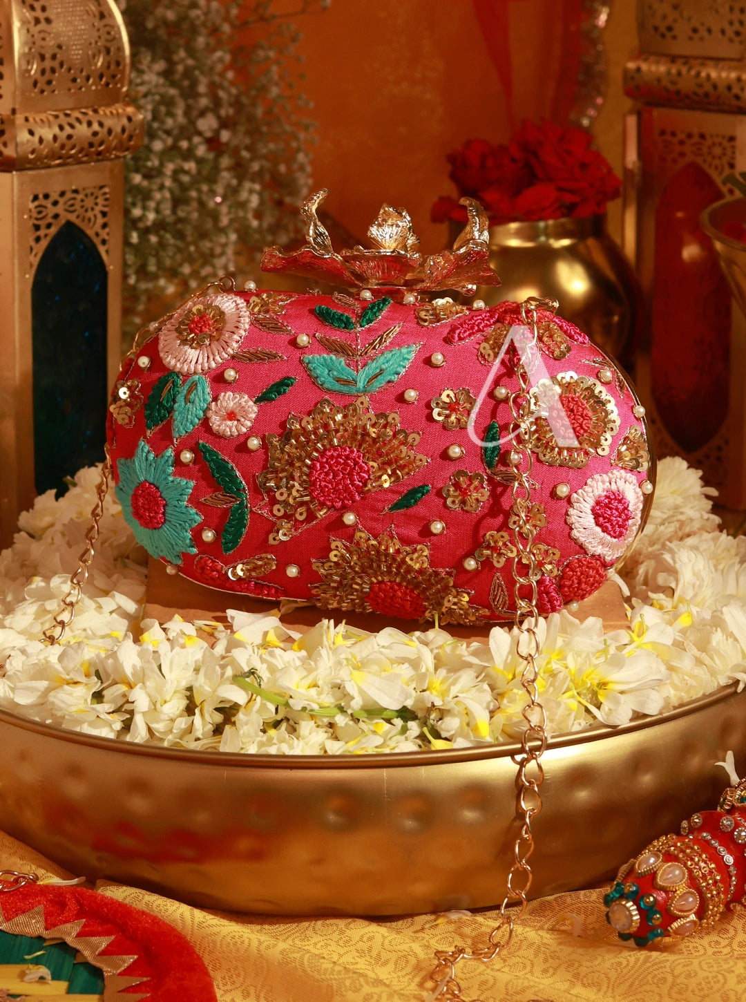 Decorative pink handbag with floral patterns on a decorative stand with flowers and a gold lantern in the background.
