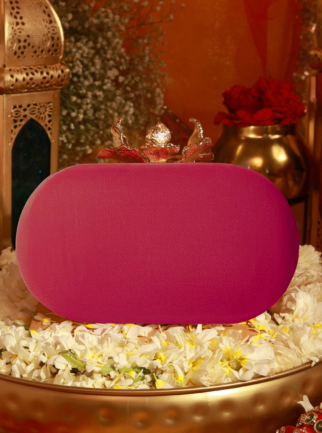 Pink clutch bag on a decorative surface with flowers and lanterns in the background