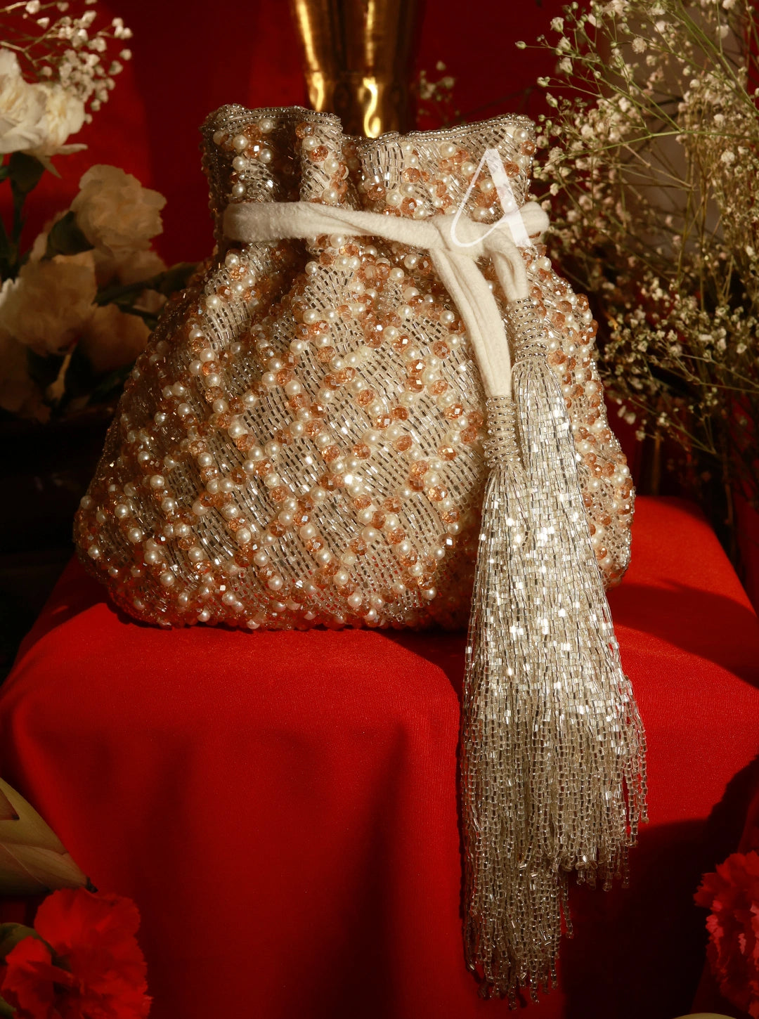 Decorative bag with beads and tassel on a red surface with flowers in the background