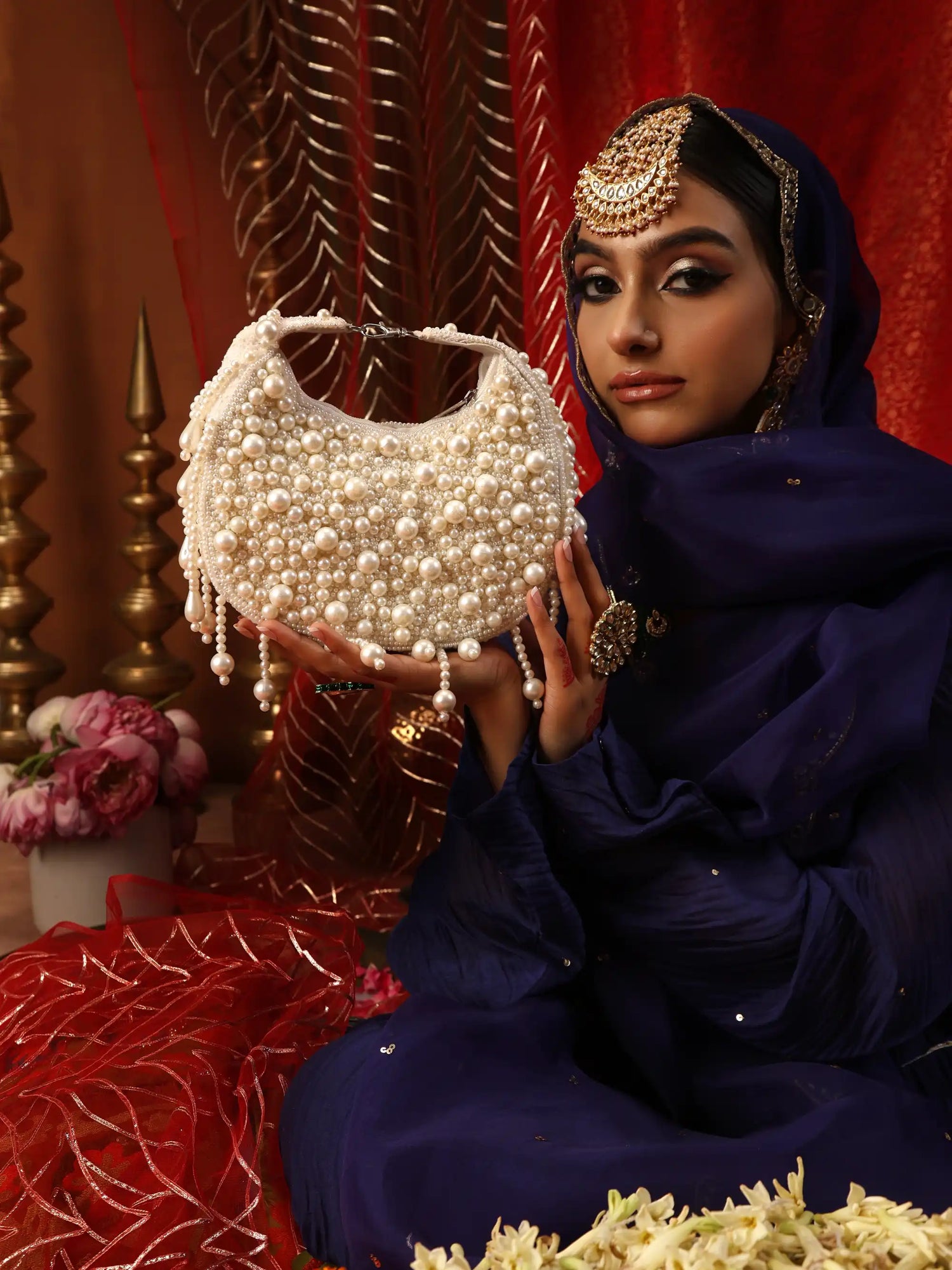 Woman in traditional attire holding a pearl-handled bag against a decorative background