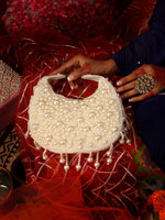 Pearl-handled handbag held by a person on a red fabric background