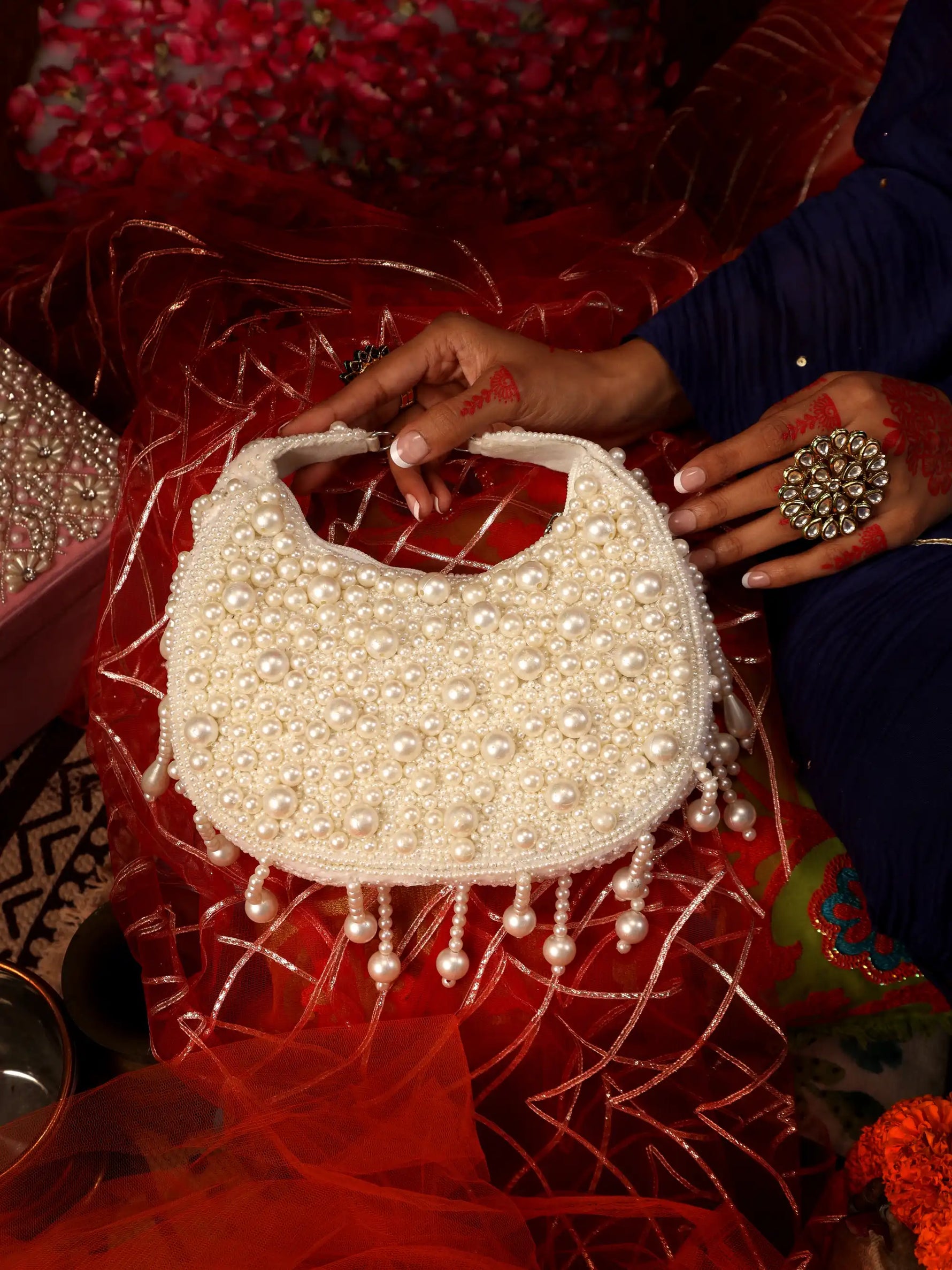 Pearl-handled handbag held by a person on a red fabric background
