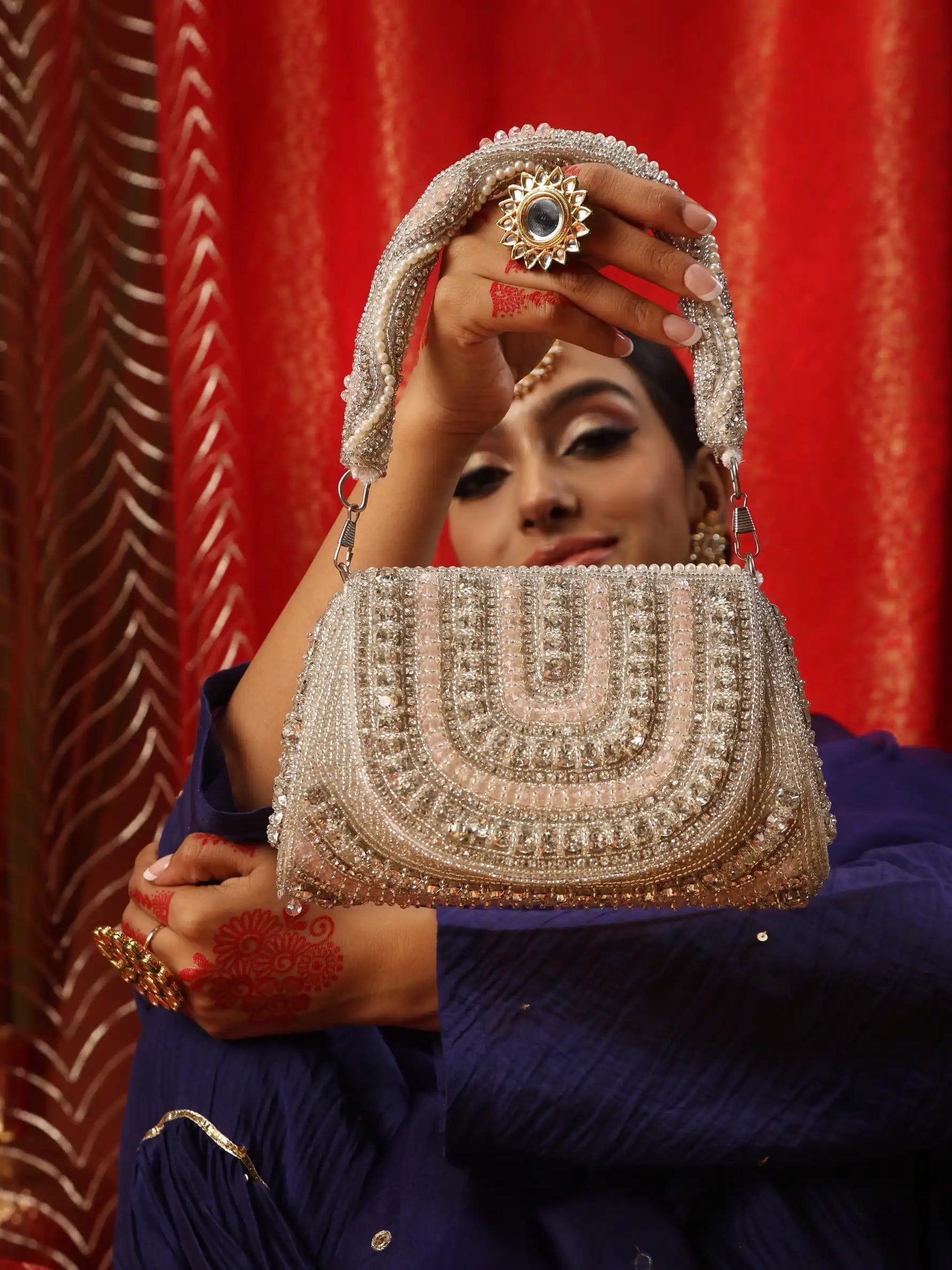 Woman holding a intricately designed handbag against a red curtain background