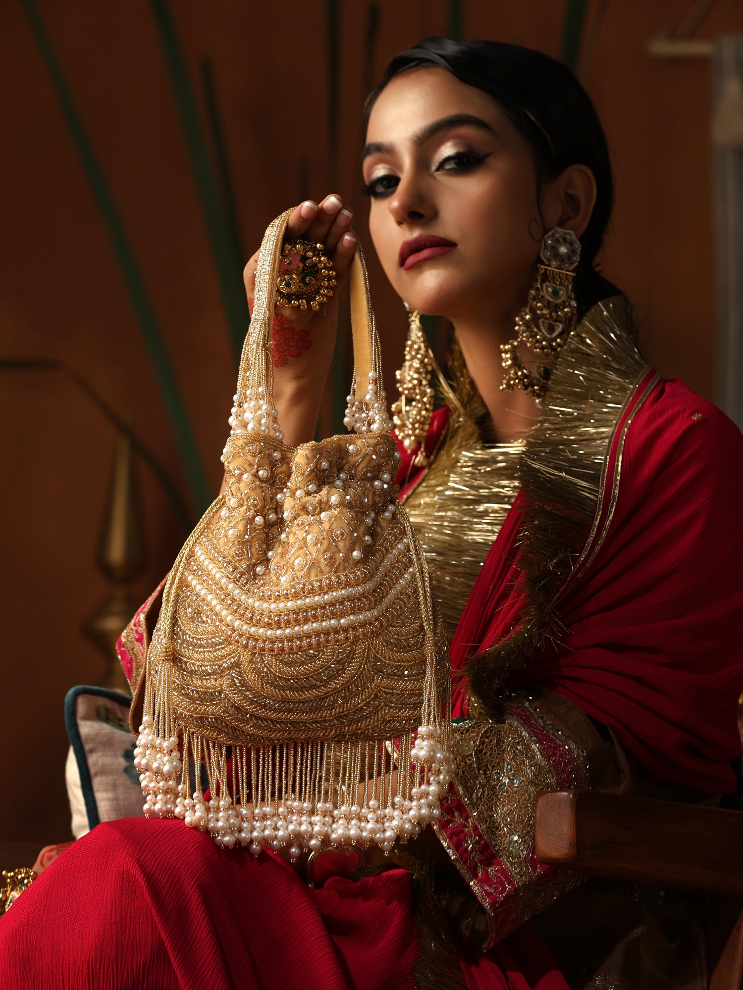 Woman in traditional attire holding a gold and pearl embellished bag.